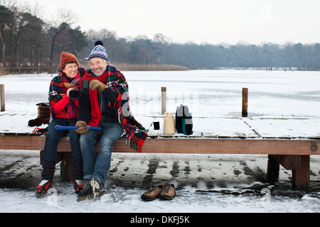 Couple sitting on pier having hot drink Stock Photo