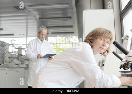 Scientists working in laboratory, woman with microscope and man taking notes Stock Photo