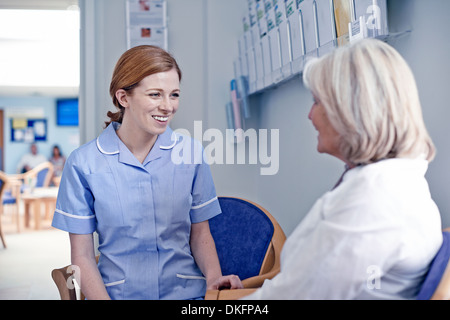 Female patient sitting with nurse in hospital waiting room Stock Photo