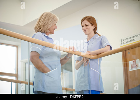 Two female nurses chatting on hospital atrium balcony Stock Photo