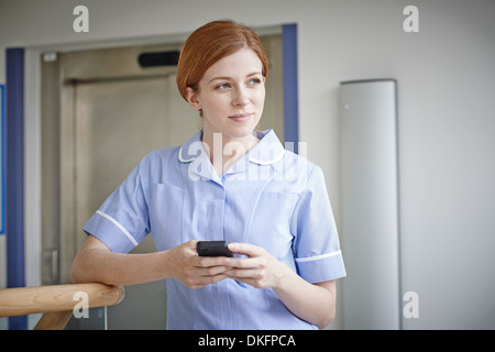 Female nurse with mobile phone outside hospital lift Stock Photo