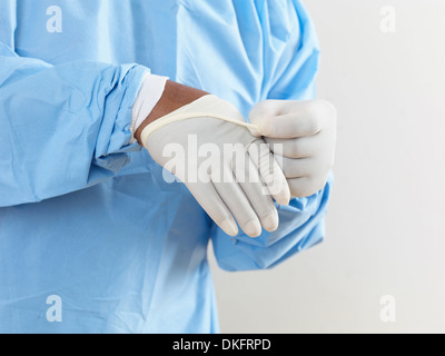 Mid section of surgeon wearing surgical scrubs putting on latex gloves Stock Photo