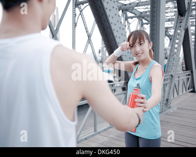 Male jogger passing water bottle to female companion Stock Photo