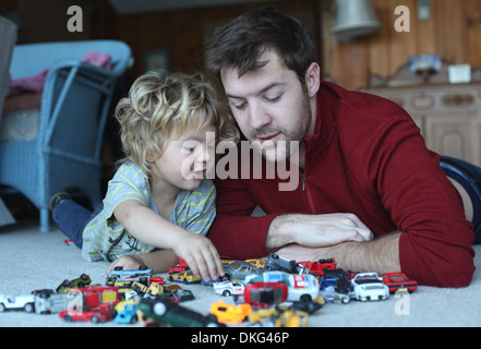 Father and toddler daughter playing with toy cars in sitting room