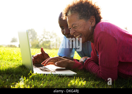 Senior couple lying in park using laptop Stock Photo