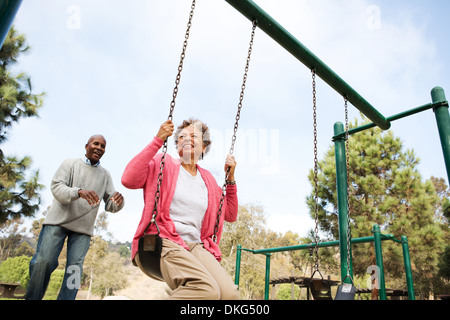 Senior man pushing woman on swing in park Stock Photo