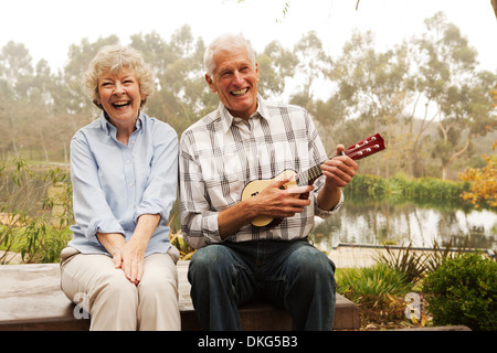 Husband playing the ukelele with wife by lake Stock Photo