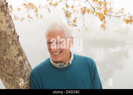 Senior man smiling and leaning against tree Stock Photo