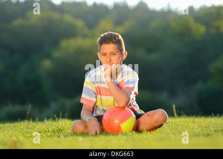 Teeange boy sitting with football on meadow, Upper Palatinate, Germany, Europe Stock Photo