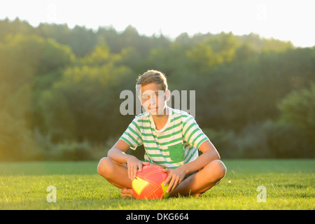 Teeange boy sitting with football on meadow, Upper Palatinate, Bavaria, Germany, Europe Stock Photo