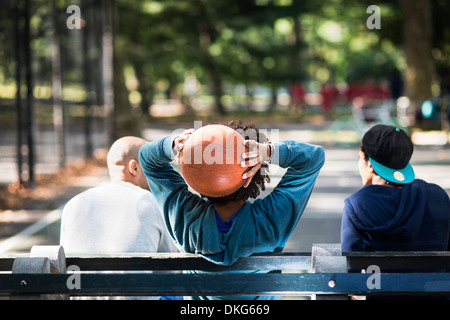 Young men sitting on park, one holding basketball Stock Photo