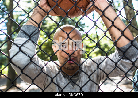 Portrait of young man holding basketball through wire fence Stock Photo