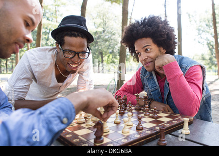 Three young men playing chess in park Stock Photo