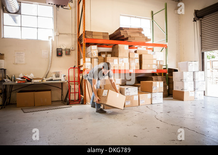 Male worker bending and lifting box in warehouse, with white cargo van ...