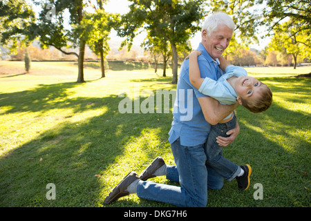 Grandfather kneeling on grass hugging grandson Stock Photo