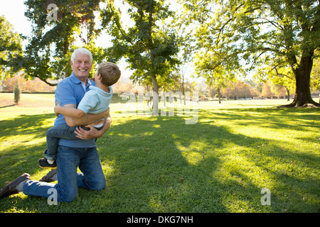 Grandfather kneeling on grass hugging grandson Stock Photo