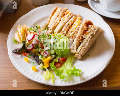 Lunchtime snack Cheddar cheese and tomato chutney sandwich in granary bread with mixed salad and Coleslaw in a café Stock Photo