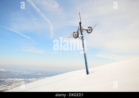 Old and weathered pillar of  an abandoned skilift line in candid ski slope covered by thick powder snow with wide panorama. Loca Stock Photo