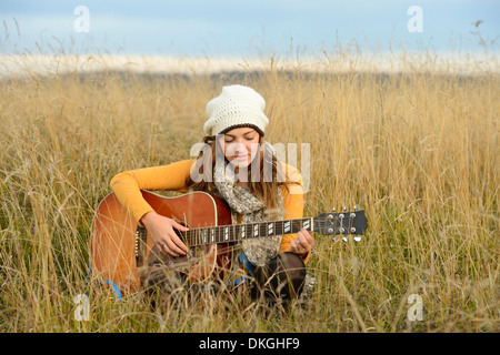 Young woman playing guitar in field Stock Photo