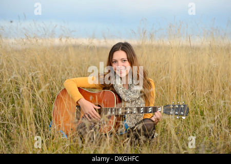 Smiling young woman playing guitar in field Stock Photo