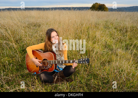 Smiling young woman playing guitar in field Stock Photo