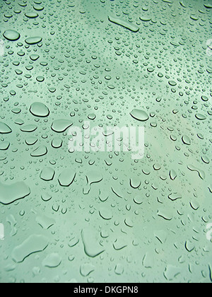 Raindrops on tinted glass panel of car sunroof against backdrop of blue sky Stock Photo