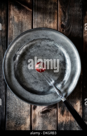 a tomato on an old silver plate, pierced by an old fork Stock Photo