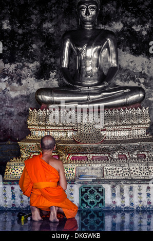 A monk prays in front of a golden Buddha, Wat Suthat, Bangkok, Thailand, Southeast Asia, Asia Stock Photo