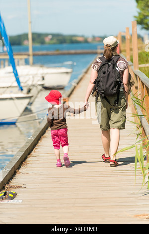 Mother and child looking at sailboats, walking on jetty on sunny summer day. Sweden. Stock Photo