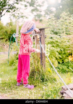 Side view of young child standing in garden helping with the watering hose Stock Photo