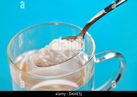 Spoon of baking soda over glass of water on blue background Stock Photo