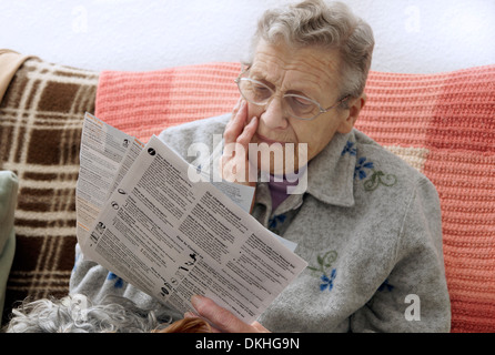 Elderly woman wearing a fleece jacket looking at electricity & gas utility bills concerned over the constant rising prices Stock Photo