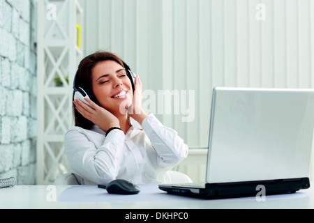 Young cheerful businesswoman listening music in headphones at office Stock Photo