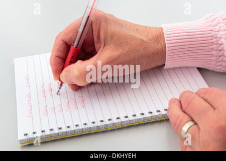 A right-handed mature woman writing a Christmas list of ideas for presents in a notebook on a tabletop. England UK Stock Photo