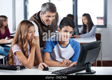 Happy Mature Teacher And Students Using Computer Stock Photo
