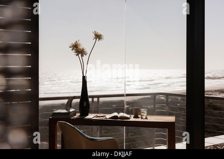 Vase of flowers on desk in modern home office overlooking ocean Stock Photo