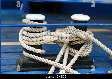 Close-up of a mooring rope with a knotted end tied around a cleat on a wooden pier/ Nautical mooring rope Stock Photo