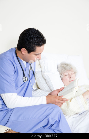 Male nurse reads book while watching elderly woman Stock Photo