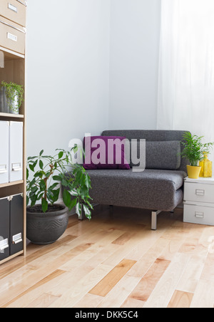 Corner of a living room with gray armchair, bookcase and plants. Stock Photo