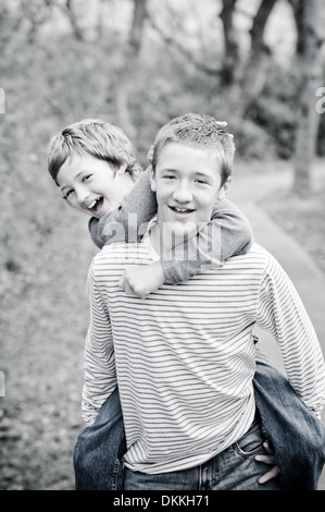 Cute brothers, teen boy giving piggyback ride outdoors, having fun - black and white Stock Photo