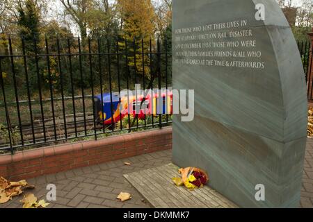 Clapham Junction, London, UK. 5th Dec, 2013.  Flowers laid at the Clapham Junction rail disaster memorial mark the 25th anniversary of the accident on December 13 as a train rushes by.  35 people were killed and  100 injured after 3 trains collided during the morning Credit:  On Sight Photographic/Alamy Live News Stock Photo