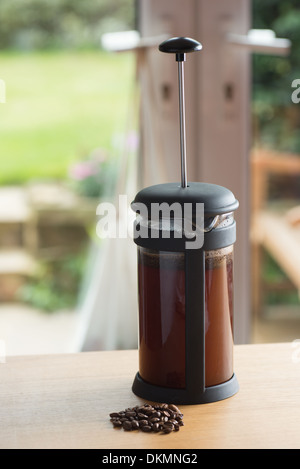 Cafetiere brewing coffee next to some coffeee beans on the kitchen table Stock Photo