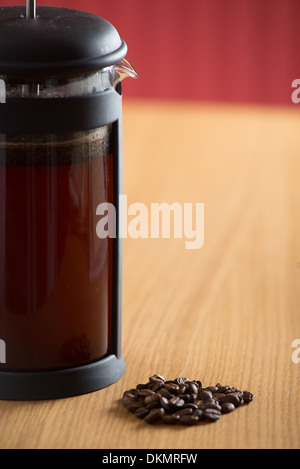 Close up of a cafetiere brewing coffee and some coffee beans on a wooden kitchen table