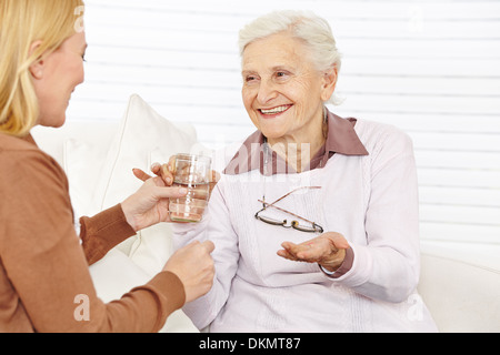 Smiling senior citizen woman taking medical pill with a cup of water Stock Photo