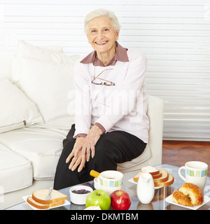 Old smiling woman sitting at set breakfast table at home Stock Photo