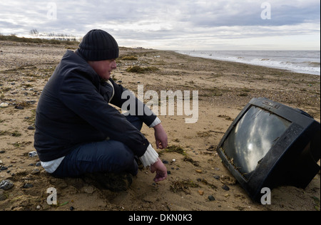 Man watching a television set washed up on a beach. Stock Photo