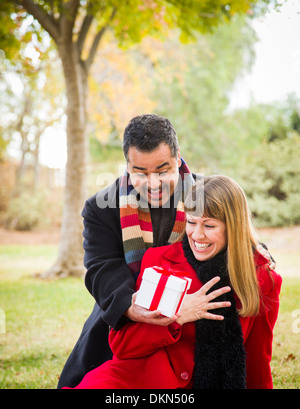 Young Attractive Mixed Race Couple Sharing Christmas or Valentines Day Gift in the Park. Stock Photo