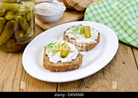 Two sandwiches with cream, pickles and dill, jar of pickles, a napkin on wooden board Stock Photo