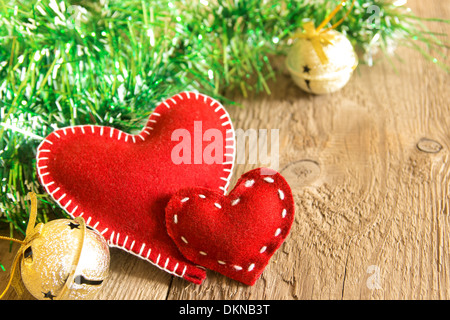 Christmas concept (decoration). Two red handmade hearts with bells over rustic wooden background (texture) close up, horizontal. Stock Photo