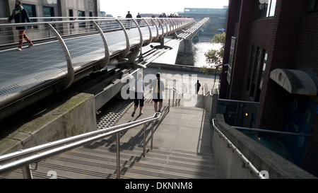 A couple of joggers running down the steps under Millennium Bridge in winter with a view of River Thames London UK  KATHY DEWITT Stock Photo